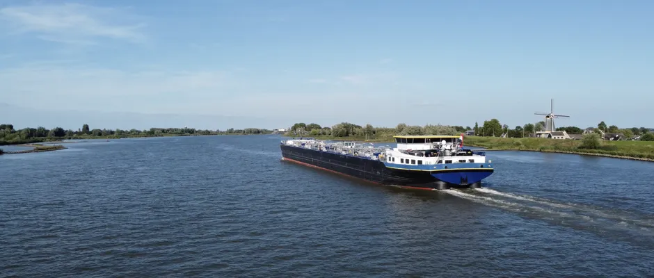 Binnenvaartschip vaart in ballast op FAME-brandstof over brede Nederlandse rivier bij heldere hemel