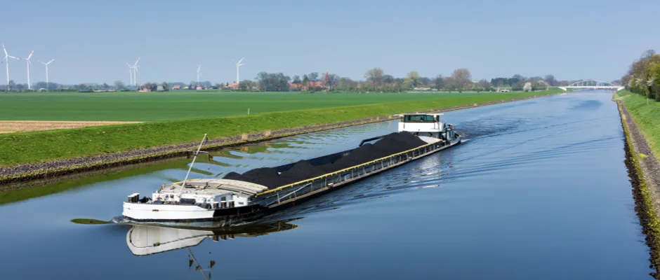 Binnenvaartschip met bulklading vaart door kanaal in landelijk gebied op HVO-brandstof