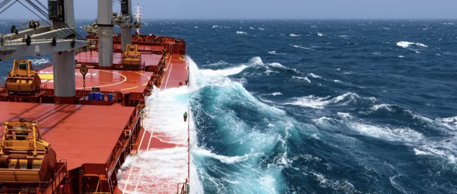 Seagoing vessel with red deck cuts through rough swell powered by bio-LNG with visible bow